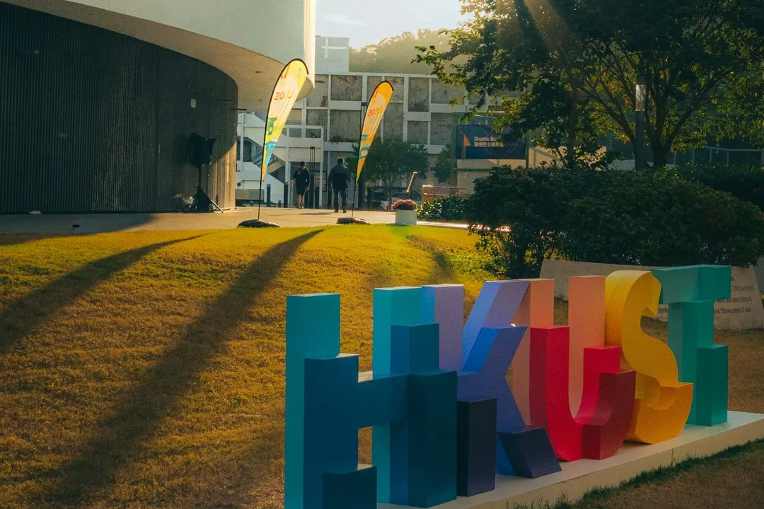 港科大草坪上的彩色 HKUST 字样标识，夕阳光线。