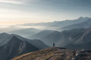 一位旅人站在山脊，远望层叠延伸的山脉。